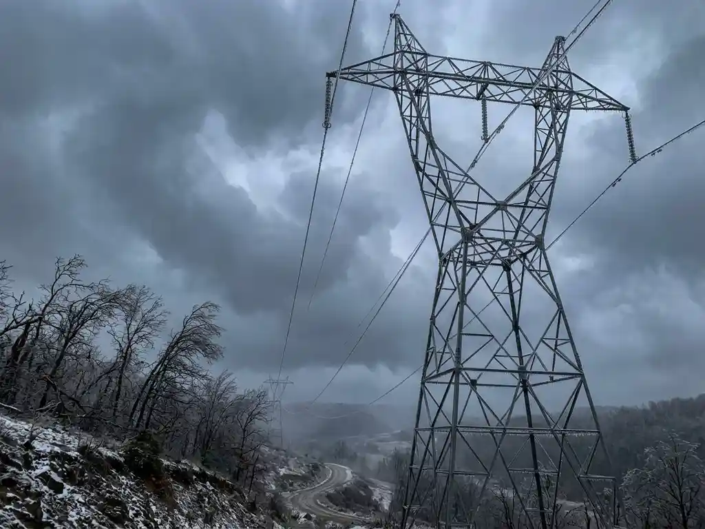 Elektrischer Hochspannungsmast mit vereisten Stromleitungen bei Sturm, dramatische Gewitterwolken am stahlgrauen Himmel