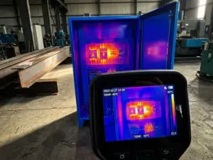 Wärmebildkamera erfasst Hitzesignaturen an elektrischem Schaltschrank mit orange-roten Hotspots an Sicherungen in Industriewerkstatt