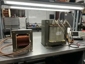 Zwei Industrietransformatoren auf Metallwerkbank, Stromwandler mit Kupferwicklungen neben Spannungswandler mit isolierten Anschlüssen
