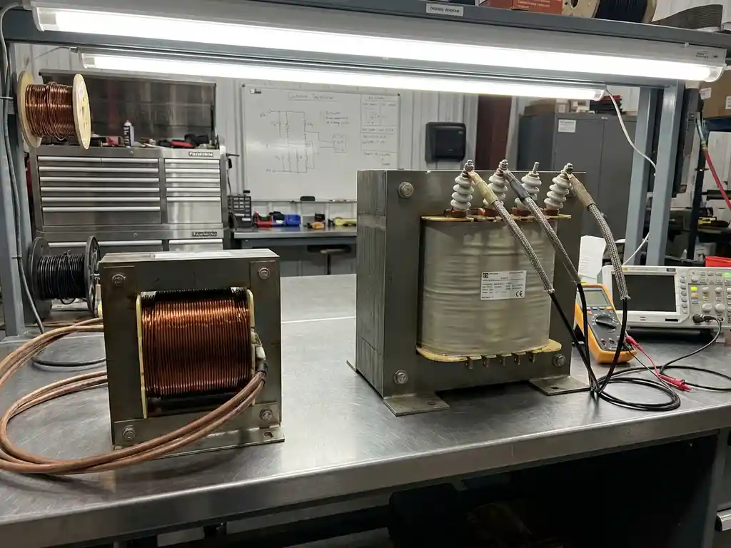Zwei Industrietransformatoren auf Metallwerkbank, Stromwandler mit Kupferwicklungen neben Spannungswandler mit isolierten Anschlüssen
